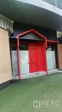 พื้นที่ขายปลีก ให้เช่าในKhlong Toei, Bangkok - ทางเข้าภายนอกกรอบหน้าจั่วสีแดง ประตูกระจกฝ้า ข้างพื้นที่หญ้าเทียม