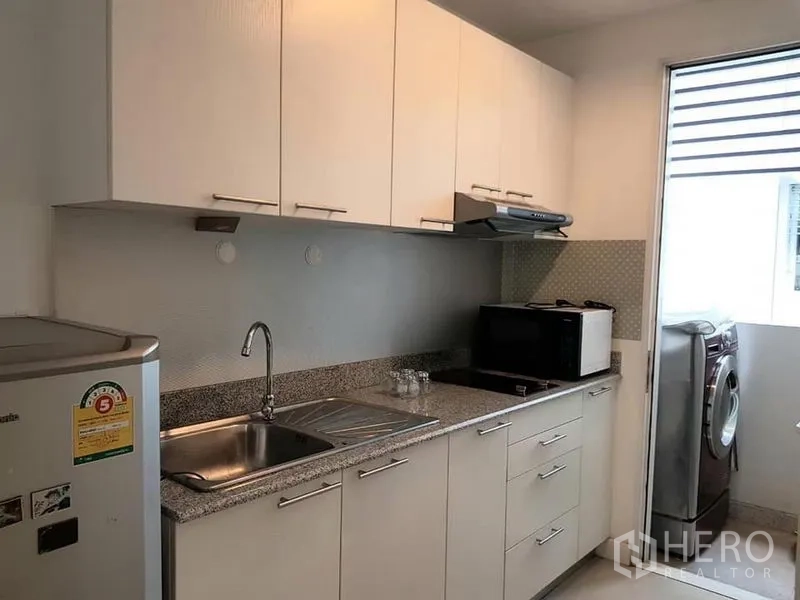 公寓 出租在Phaya Thai, Bangkok - 独立厨房，白色橱柜、花岗岩台面，带水槽、微波炉、冰箱及窗边洗衣机。