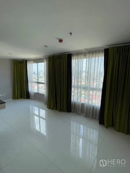 Condominium for sale in Suan Luang, Bangkok - Corner living area with floor-to-ceiling windows, green curtains and city skyline views.