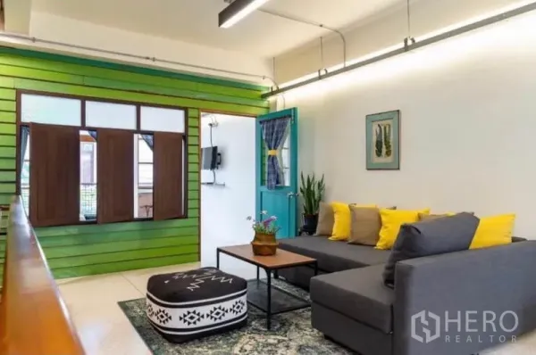 Townhouse for rent in Pathum Wan, Bangkok - Bright living room with L-shaped sofa, green accent wall and vintage shutters.