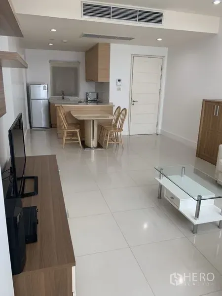 Condominium for rent or sale in Khlong Toei, Bangkok - Bright open-plan living and dining area with modern kitchenette, white tile floors and wood cabinetry.