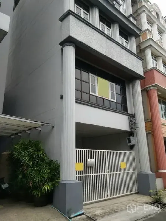 Townhouse for rent in Phra Khanong, Bangkok - Front exterior of a multi‑storey townhouse with classical columns and a gated carport.