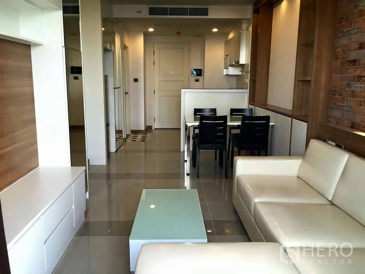 Condominium for sale in Huai Khwang, Bangkok - Open-plan living and dining area with glossy tile floors, four-seat dining set and compact kitchenette.