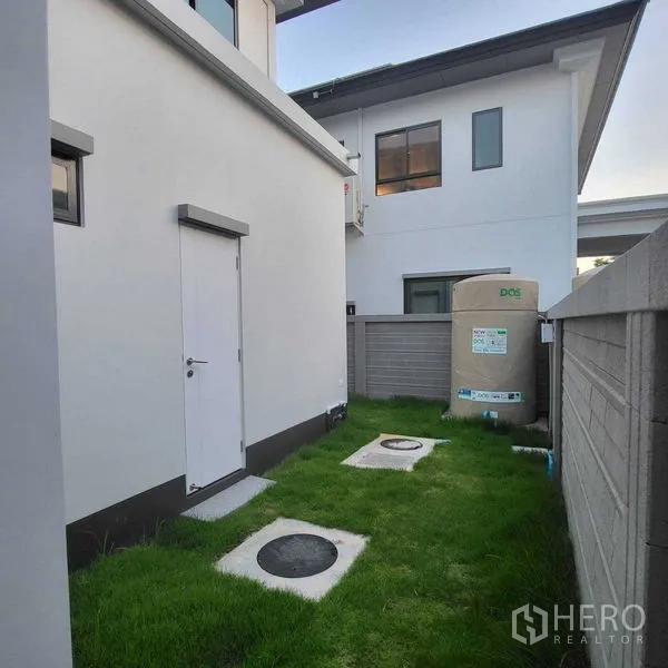 Detached House for rent in Mueang Pathum Thani, Pathum Thani - Narrow side yard with grass, utility door and water tank