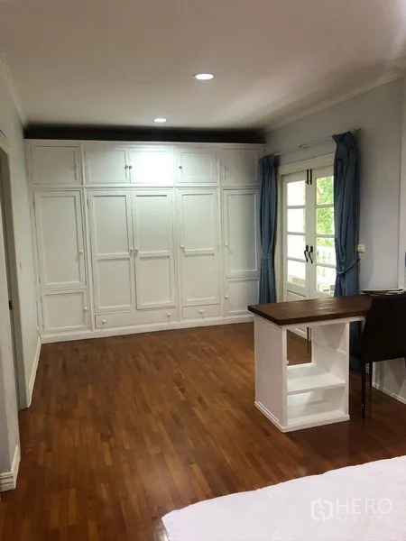 ทาวน์เฮาส์ ให้เช่าในMueang Samut Prakan, Samut Prakan - ห้องนอนกว้าง พื้นไม้ ตู้เสื้อผ้าบิวท์อินสีขาว โต๊ะทำงาน และประตูบานฝรั่งเศสพร้อมผ้าม่านสีน้ำเงิน