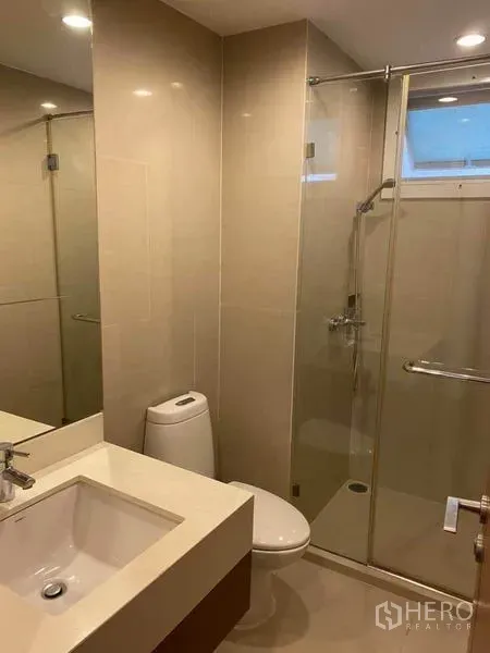 Condominium for rent in Watthana, Bangkok - Modern bathroom with glass-enclosed shower, tiled walls, and a wide vanity sink with mirror.