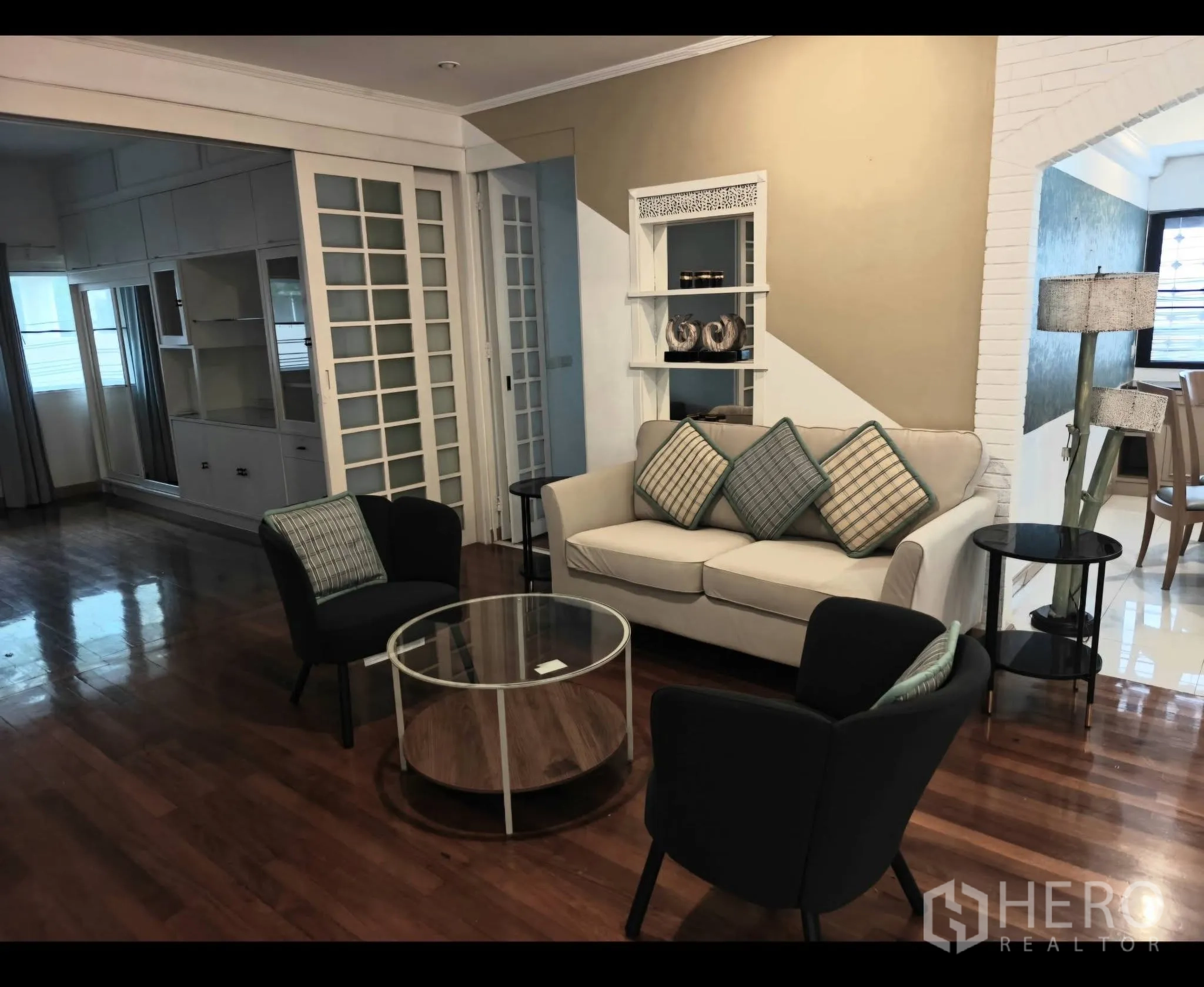 Condominium for rent in Sathon, Bangkok - Living room with sofa set, glass coffee table, wood floors, and sliding glass partitions.