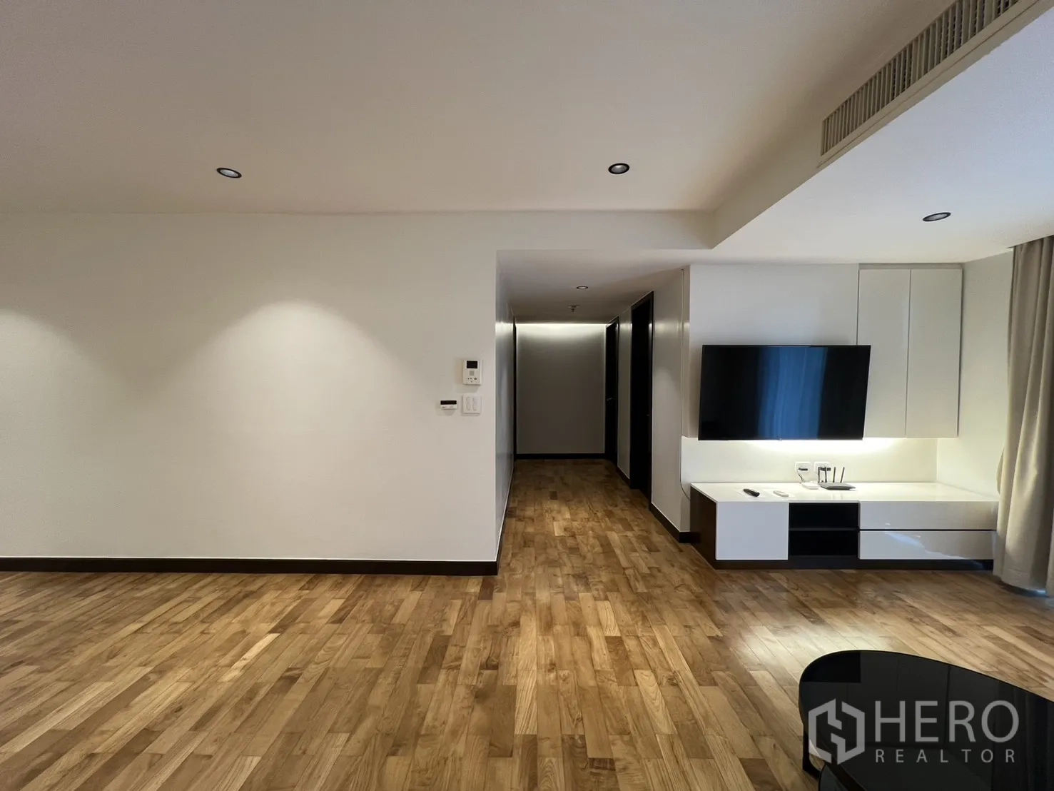 Apartment for rent in Watthana, Bangkok - View of the living room showing TV console, recessed lighting, wood flooring, and corridor to the bedrooms.