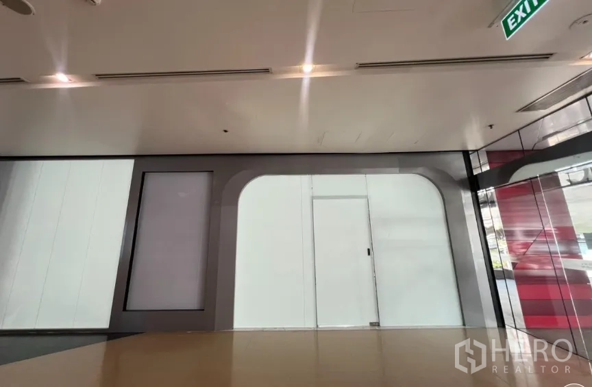 Retail Space for rent in Pathum Wan, Bangkok - Interior corridor with a glass storefront, ceiling lights, and an exit sign.