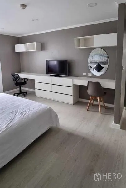 公寓 出租在Khlong Toei, Bangkok - 宽敞卧室，带一体式书桌、电视柜与圆形镜，现代灰白配色。