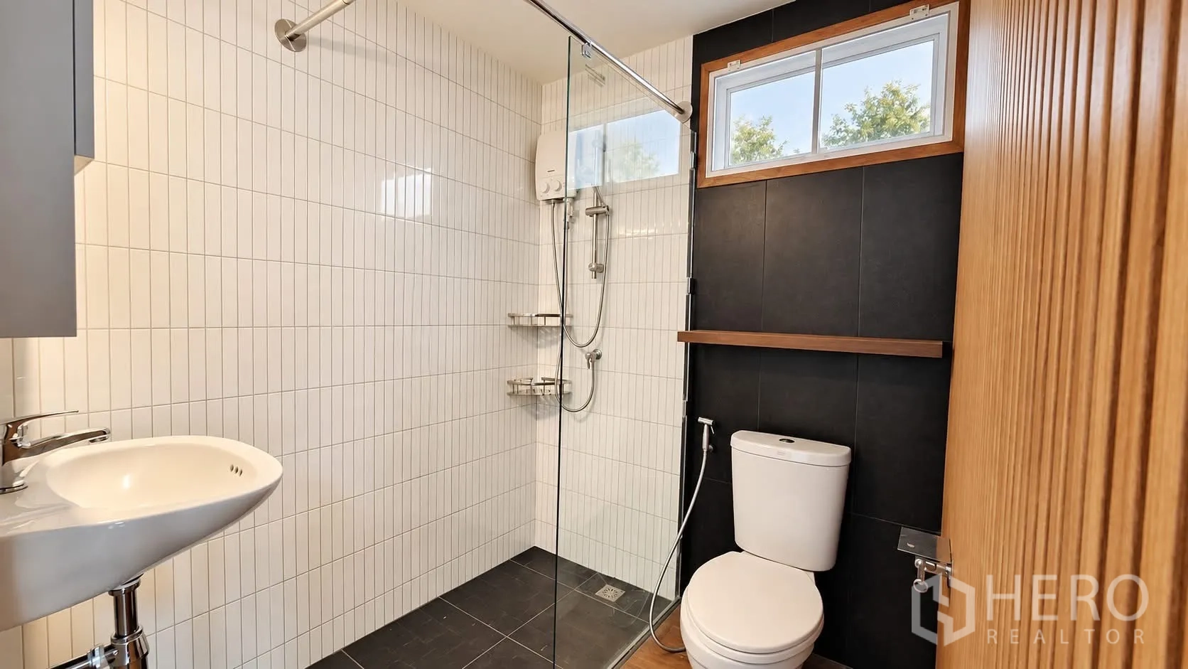 Detached House for rent in Khlong Toei, Bangkok - Bathroom with glass-enclosed walk-in shower, toilet, and vertical white tiles with dark accent wall.