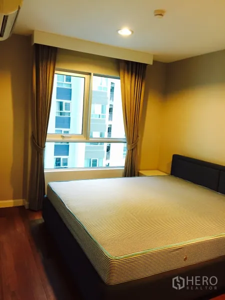 Condominium for rent in Huai Khwang, Bangkok - Bright bedroom with a large bed, curtains and a city-view window.