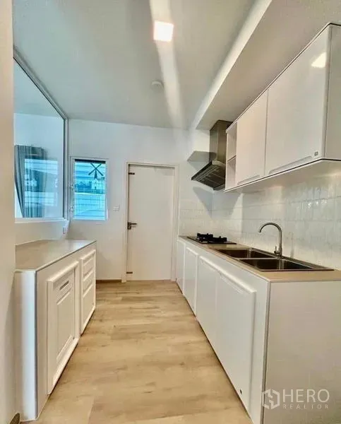 Townhouse for rent in Bang Phli, Samut Prakan - Galley kitchen featuring white cabinetry, double sink, gas hob and range hood.