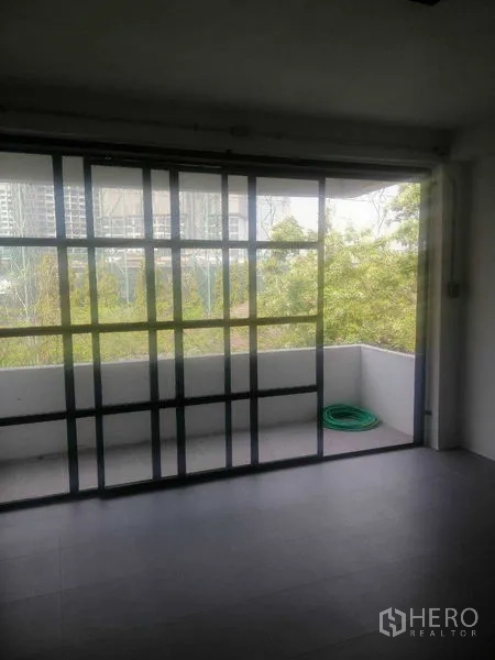 Shophouse for rent in Khlong Toei, Bangkok - Balcony area with hose and tree views through black-framed glass.