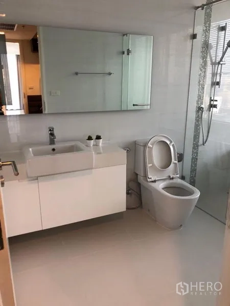 Condominium for rent in Sathon, Bangkok - Bathroom with wide vanity and mirror, toilet and glass‑partitioned shower area.