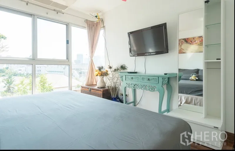 Condominium for rent in Pathum Wan, Bangkok - Master bedroom with wall-mounted TV, decorative console and city view through wide windows.
