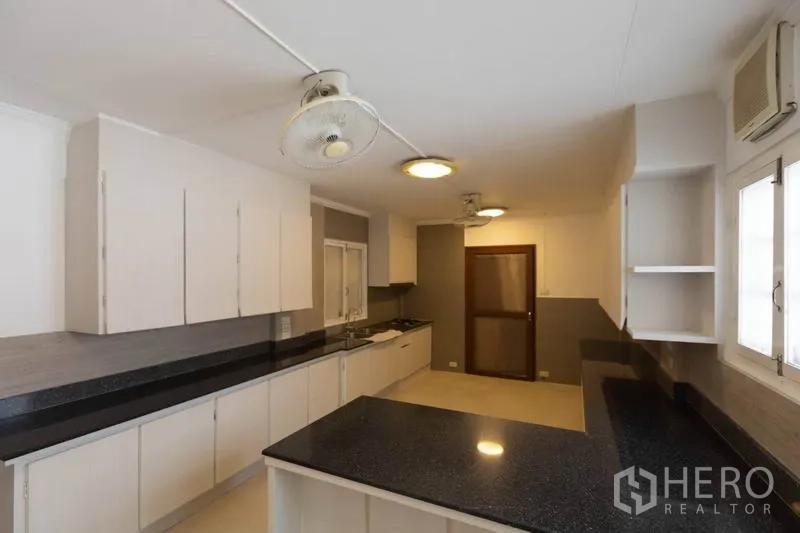 Detached House for rent in Pathum Wan, Bangkok - Large kitchen featuring black stone countertops, ample white cabinetry and windows.