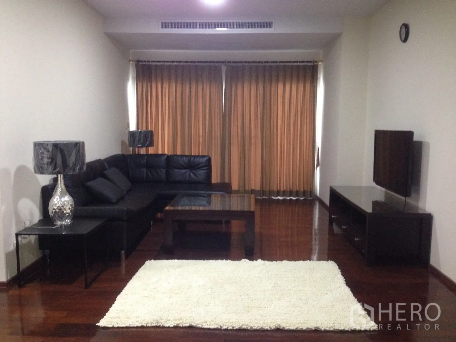 คอนโด ให้เช่าในWatthana, Bangkok - ห้องนั่งเล่นมีโซฟาหนังรูปตัวแอลสีดำ ชั้นวางทีวี และผ้าม่านบานใหญ่