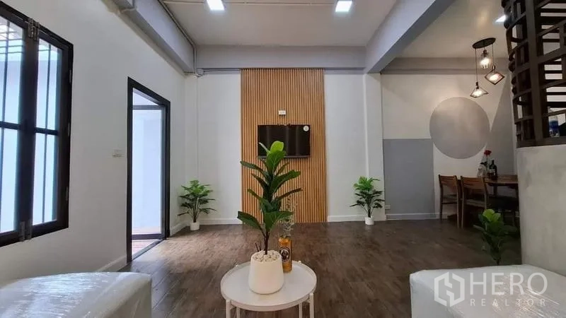 ทาวน์เฮาส์ ให้เช่าหรือขายในChatuchak, Bangkok - พื้นที่นั่งเล่นมีผนังทีวีลายซี่ไม้ ไม้กระถาง และมุมทานอาหาร พื้นไม้