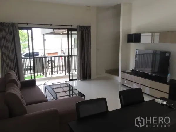Townhouse for rent or sale in Saphan Sung, Bangkok - Bright living and dining area with sofa, TV console and sliding glass doors opening to a covered terrace.