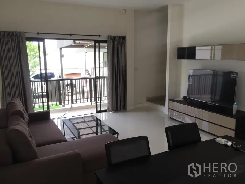 Townhouse for rent or sale in Saphan Sung, Bangkok - Bright living and dining area with sofa, TV console and sliding glass doors opening to a covered terrace.