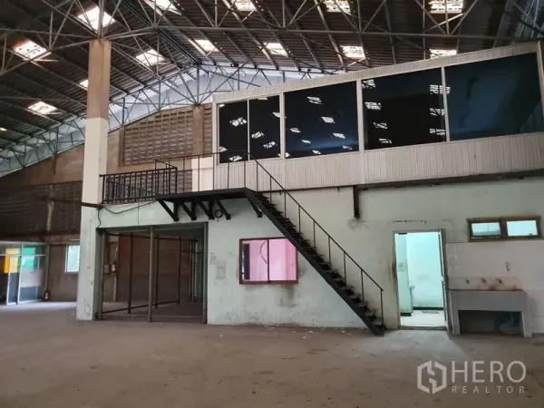 Factory for rent in Samut Prakan - Mezzanine glass office with metal staircase above ground-floor rooms and a service sink inside the factory.