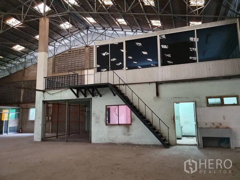 Factory for rent in Samut Prakan - Mezzanine glass office with metal staircase above ground-floor rooms and a service sink inside the factory.