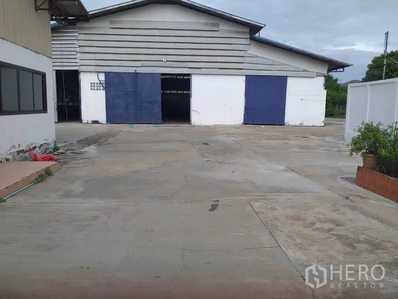 Warehouse for rent in Pak Kret, Nonthaburi - Warehouse exterior in Pak Kret with blue-and-white sliding doors and a large concrete loading yard.