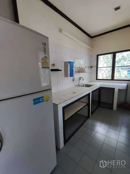 Detached House for rent in Khlong Toei, Bangkok - Practical Thai kitchen with tiled counters, sink, open shelving and refrigerator by the window.