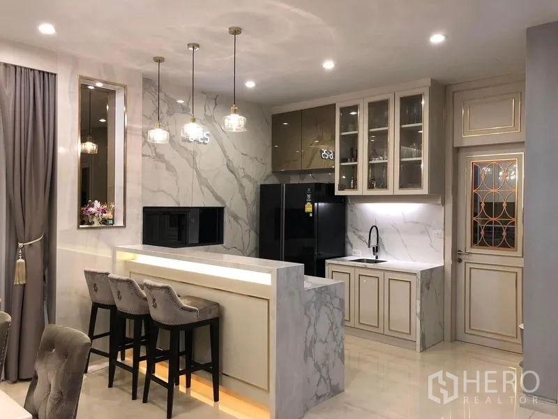 Detached House for rent or sale in Prawet, Bangkok - Marble-finished kitchen with island breakfast bar, pendant lights, and built-in cabinets.