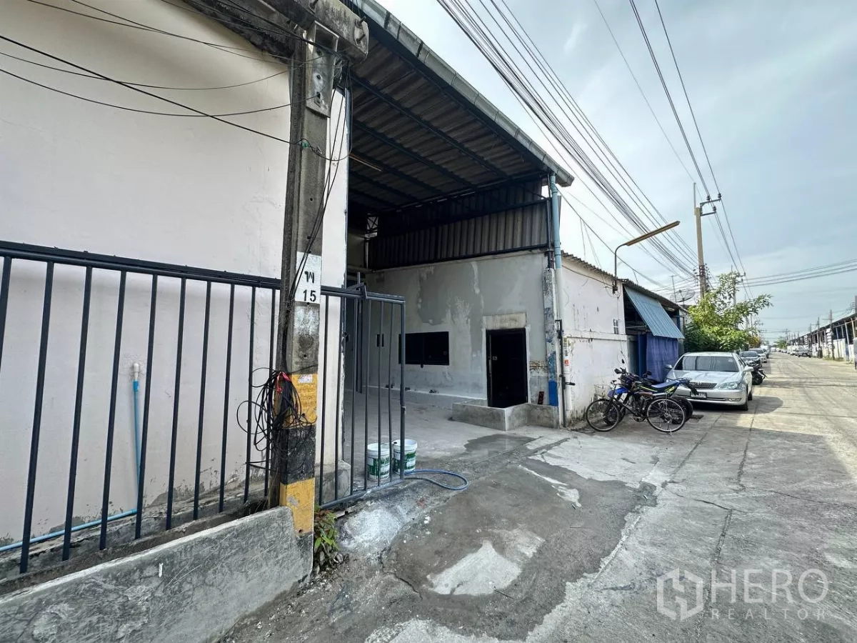 โรงงาน ให้เช่าในSamut Prakan - ด้านหน้าโกดังติดถนนซอย มีประตูบานเลื่อน พื้นคอนกรีตและเสาไฟฟ้าในย่านอุตสาหกรรม บางพลี