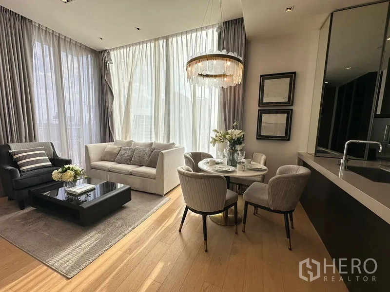 Condominium for rent in Pathum Wan, Bangkok - Dining nook beside the living area with chandelier, sofa and large sheer curtains.