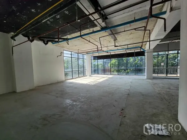 Retail Space for rent in Sathon, Bangkok - Sunlit shell retail corner with floor-to-ceiling windows, exposed pipes and concrete floor overlooking greenery.