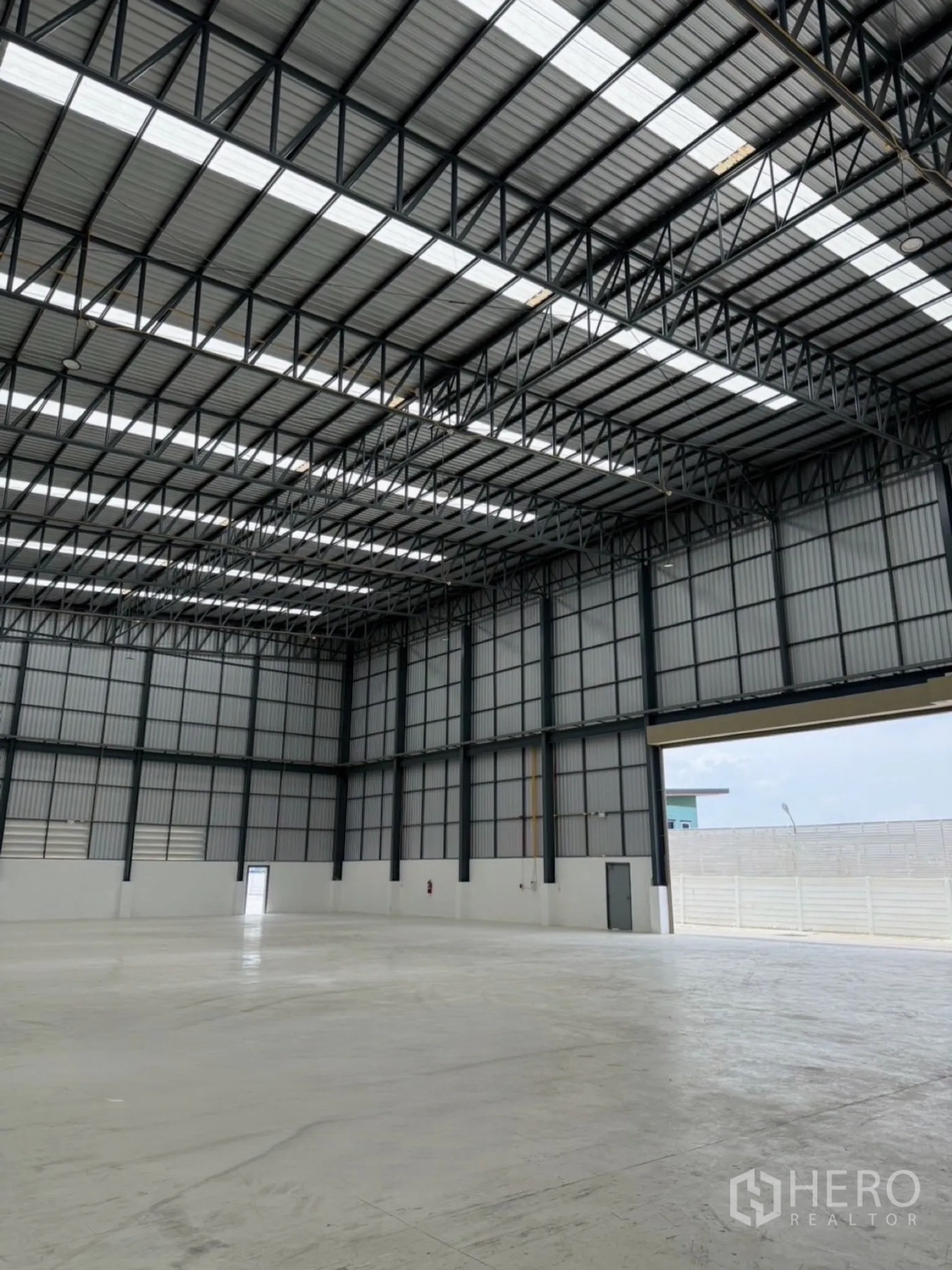 Factory for sale in Ban Bueng, Chon Buri - Spacious warehouse interior with high steel truss roof, skylights, and polished concrete floor.