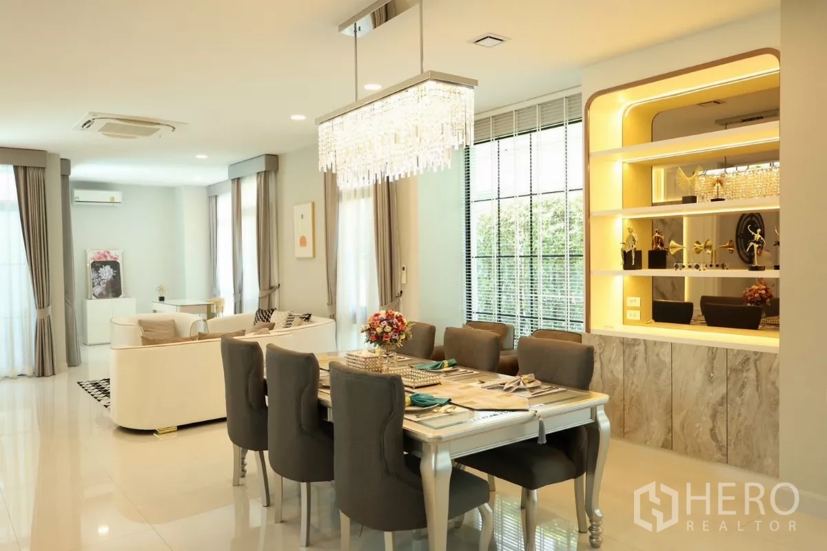 Detached House for rent or sale in Saphan Sung, Bangkok - Open-plan living and dining area with crystal chandelier, large windows, and illuminated built-ins.