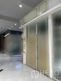 Retail Space for rent in Khlong Toei, Bangkok - Hallway view of small retail shop with frosted glass frontage, metal handles, recessed ceiling lights, and polished white floors.
