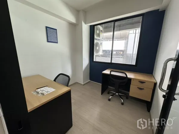Office Space for rent in Watthana, Bangkok - Compact two-desk office with a large window, navy feature wall and laminate flooring.