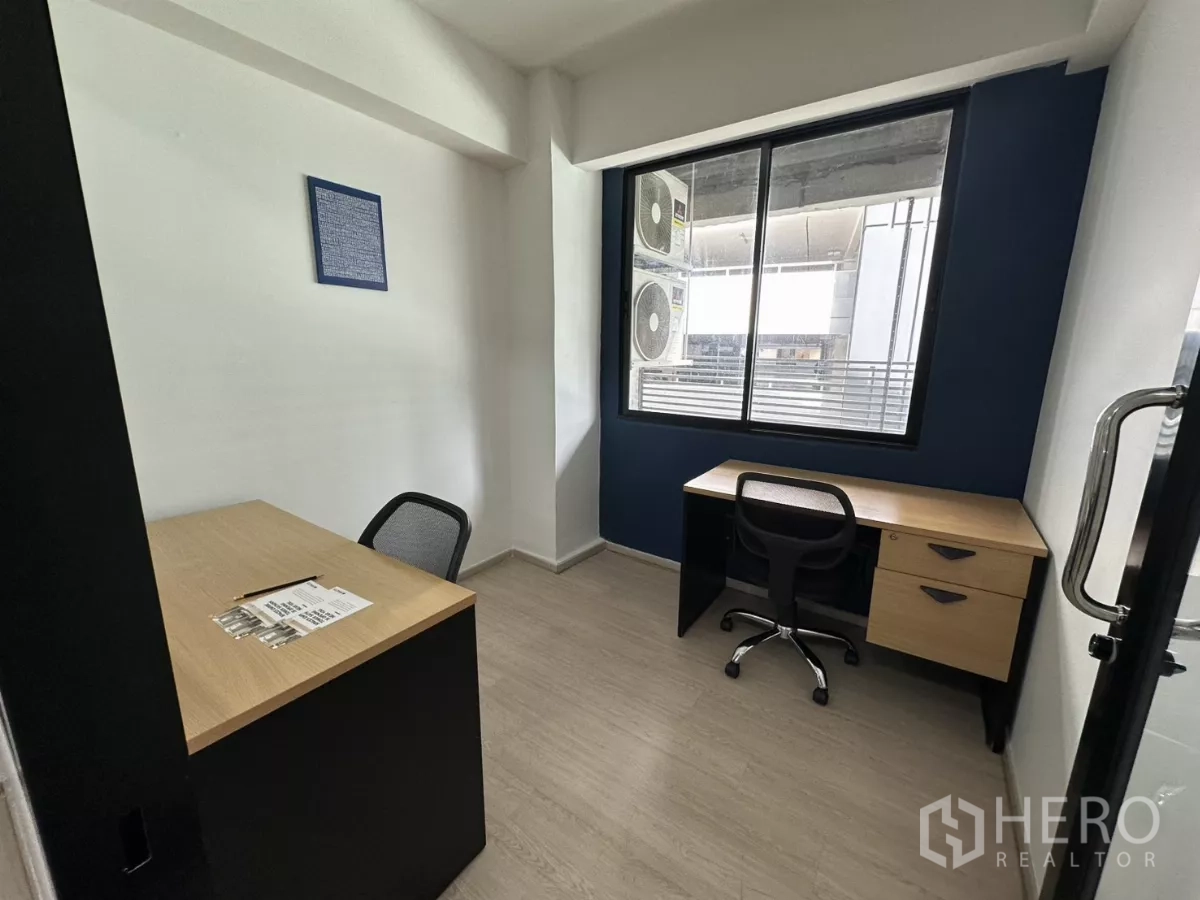 Office Space for rent in Watthana, Bangkok - Compact two-desk office with a large window, navy feature wall and laminate flooring.