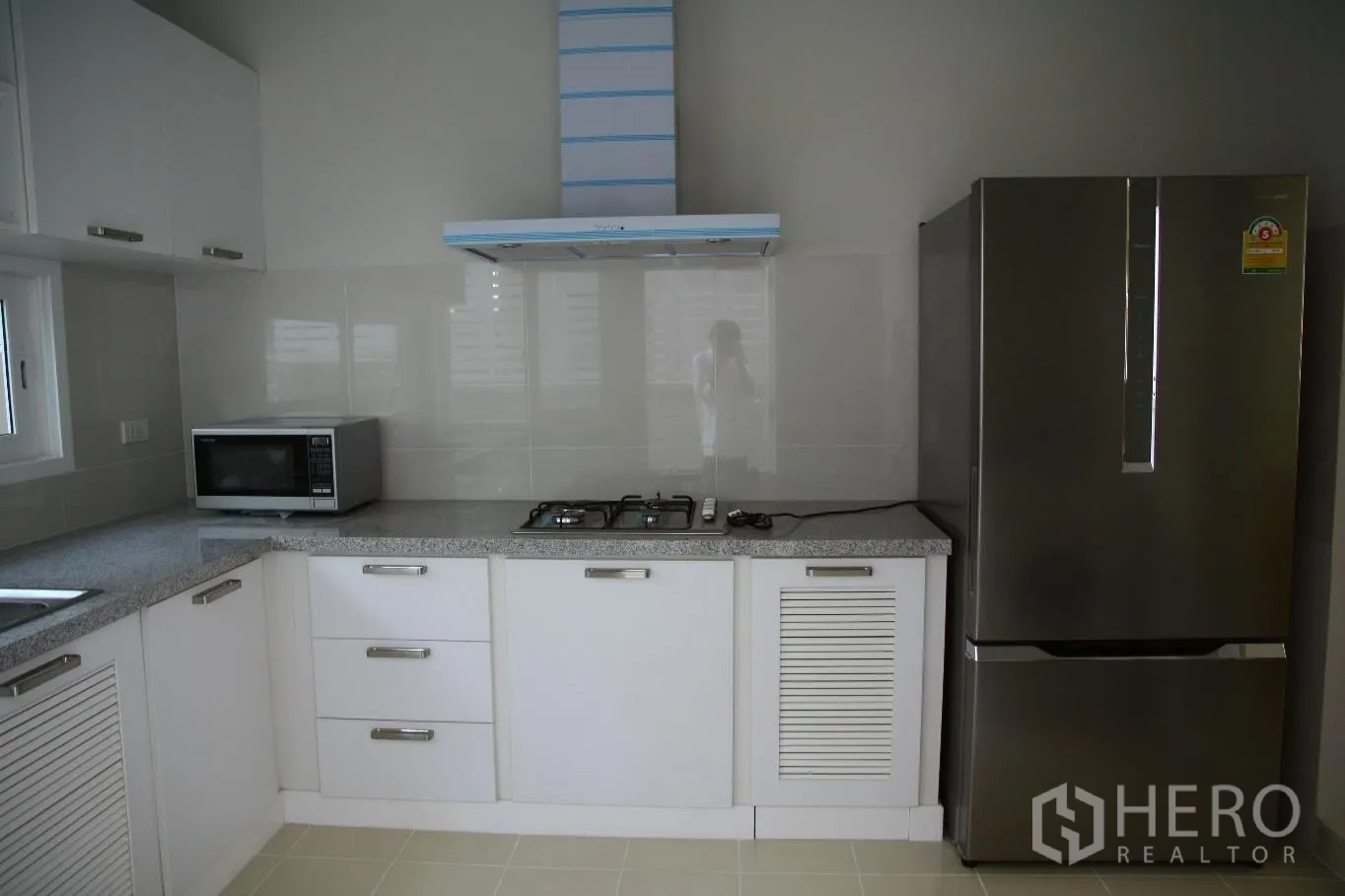 Detached House for rent or sale in Bang Na, Bangkok - Fitted kitchen with white cabinets, granite countertop, gas hob, range hood, microwave and stainless refrigerator.
