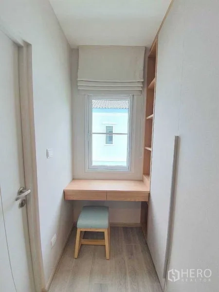 Townhouse for rent - Compact study nook by a window with wooden desk, shelves, and a small stool.