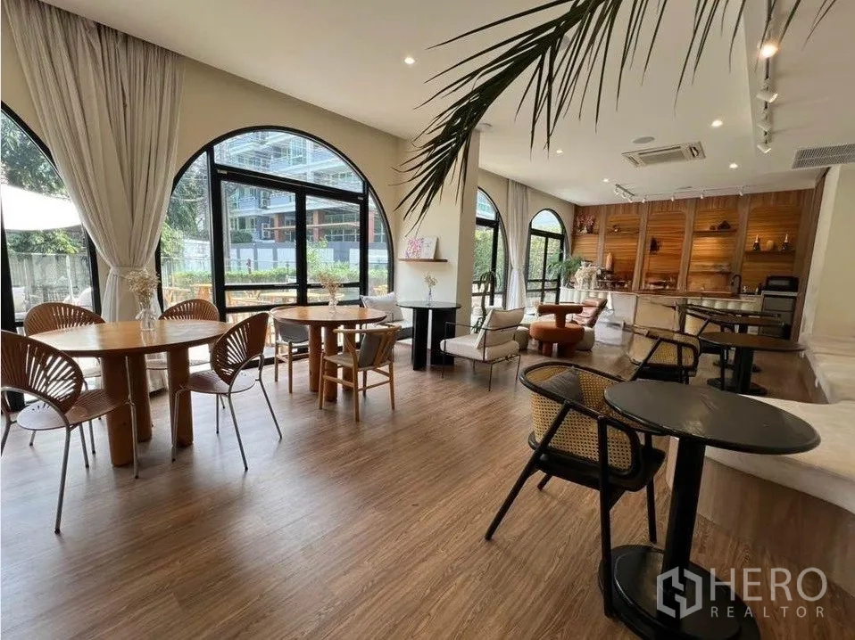 零售空间 出租在Watthana, Bangkok - 开放式零售空间，多处桌椅、暖色灯光与拱形玻璃及木地板。