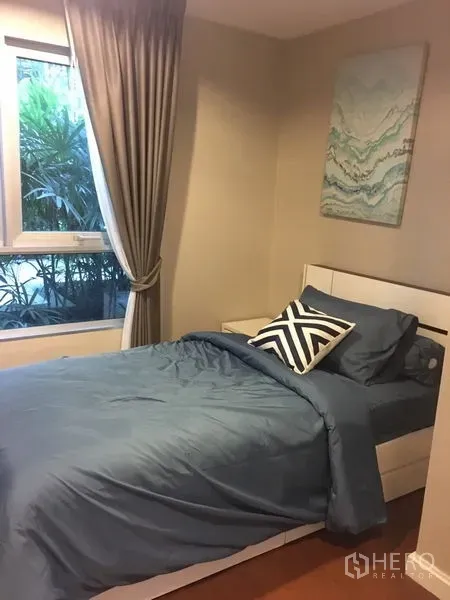 Condominium for rent or sale in Huai Khwang, Bangkok - Cozy single bedroom with blue bedding, window and floor-length curtains.
