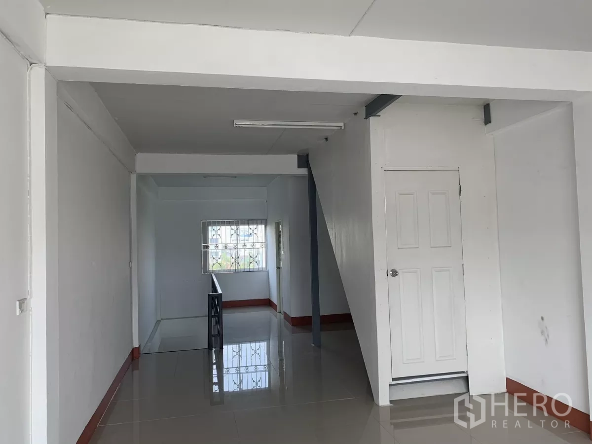 Home Office for rent in Lat Krabang, Bangkok - Long open‑plan space with stairwell partition, white door and natural light from rear window.