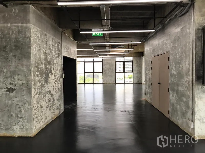 Office Space for rent in Khlong Toei, Bangkok - Entry corridor of an industrial-style office with textured concrete walls, exit sign, and full-height windows ahead.