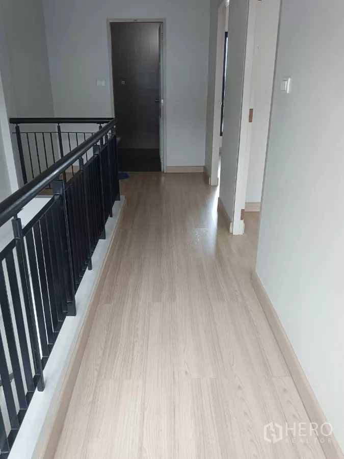 联排别墅 出租在Mueang Samut Prakan, Samut Prakan - 二楼走廊，浅木地板与黑色金属扶手，旁有卫生间门。