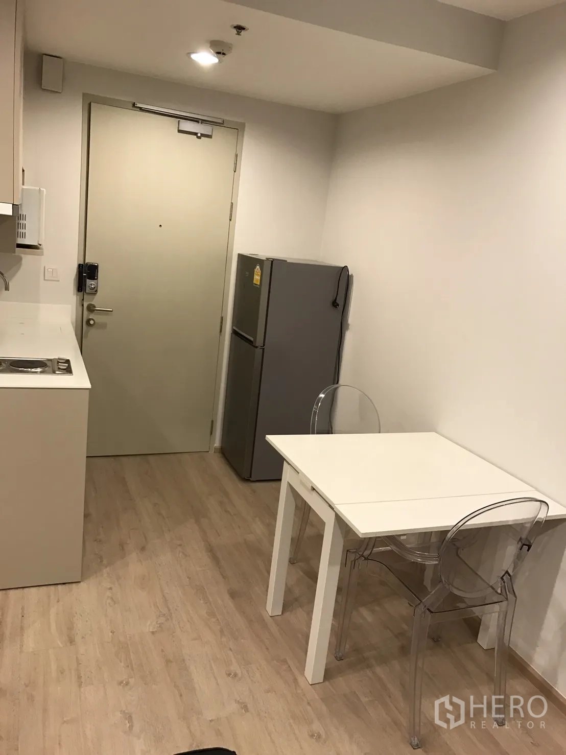 公寓 出租或出售在Ratchathewi, Bangkok - 紧凑厨房，配冰箱与白色餐桌和透明椅，靠近入户门