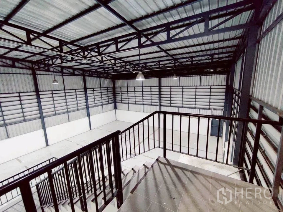 Warehouse for rent in Lam Luk Ka, Pathum Thani - View from mezzanine railing over expansive warehouse hall and lighting.