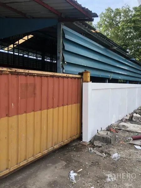 Warehouse for rent in Samut Prakan - Warehouse exterior with blue metal cladding, white perimeter wall and a large sliding metal gate for vehicle access.