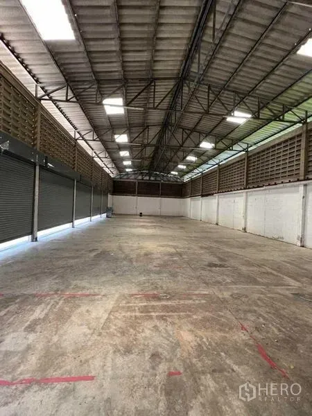 货栈 出租在Bang Na, Bangkok - 仓库内部为大开间，高钢梁屋顶配采光窗，水泥地面，侧墙设多扇卷帘门。