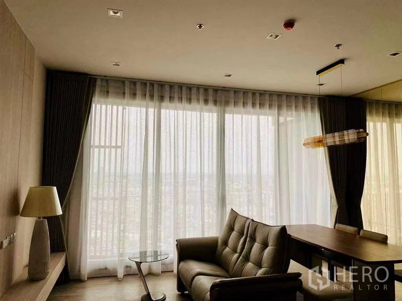 คอนโด ให้เช่าในBang Kho Laem, Bangkok - ห้องนั่งเล่นบรรยากาศสบาย โซฟาและโต๊ะทำงานรับวิวเมืองผ่านผ้าม่านโปร่งเต็มผนัง